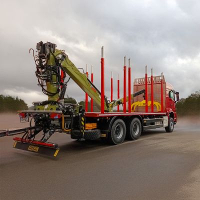 Red timber transport truck with a green loading crane and red stakes, ready for wood transport.