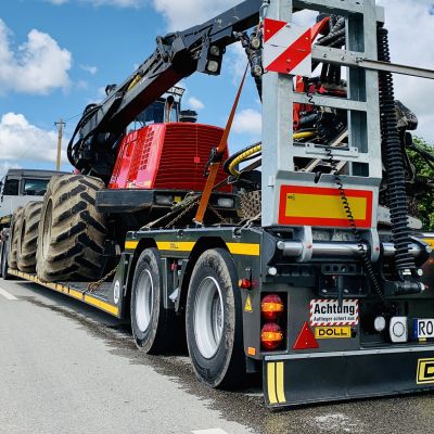 La remorque forestière surbaissée DOLL sur la route, chargée d'une machine forestière