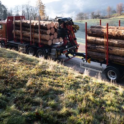 Truck with DOLL central axle trailer drives along a narrow country road between meadows and fields at dawn