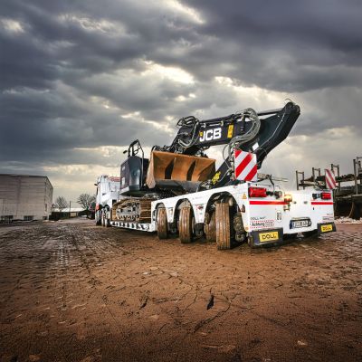 Pelleteuse stationnée sur une remorque surbaissée pour transport lourd sous un ciel dramatique.