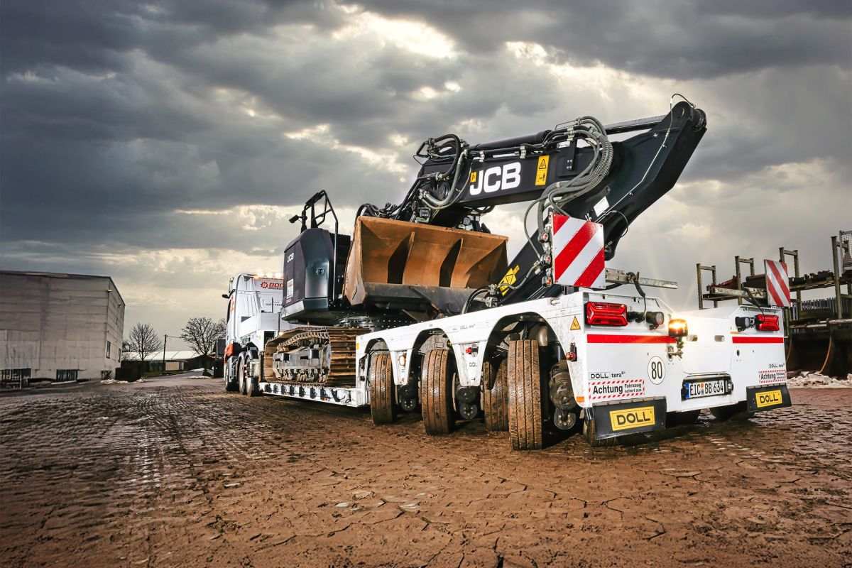 Bagger auf einem Tieflader für den Schwertransport unter dramatischem Himmel geparkt.