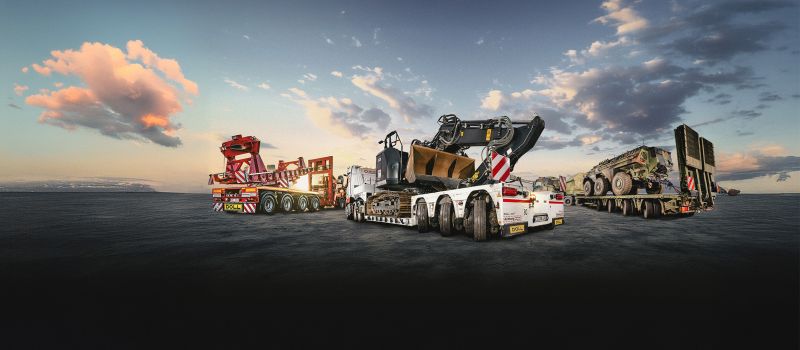 Heavy haulage with low-loaders carrying construction and military vehicles under a dramatic sky.