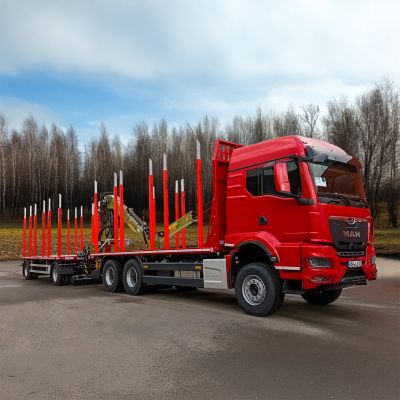 Red timber transport truck with a DOLL platfporm trailer, red stakes, and a loading crane in a forested area.